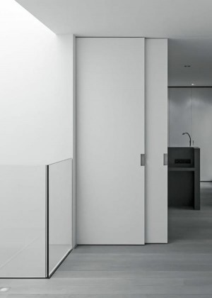 Мінімалістичний інтер'єр із білими розсувними дверима, сучасною кухнею в темних тонах і світлою дерев'яною підлогою