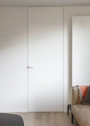 Гостиная в скандинавском стиле с бежевым диваном, пледом в полоску, и белой встроенной дверью скрытого монтажа