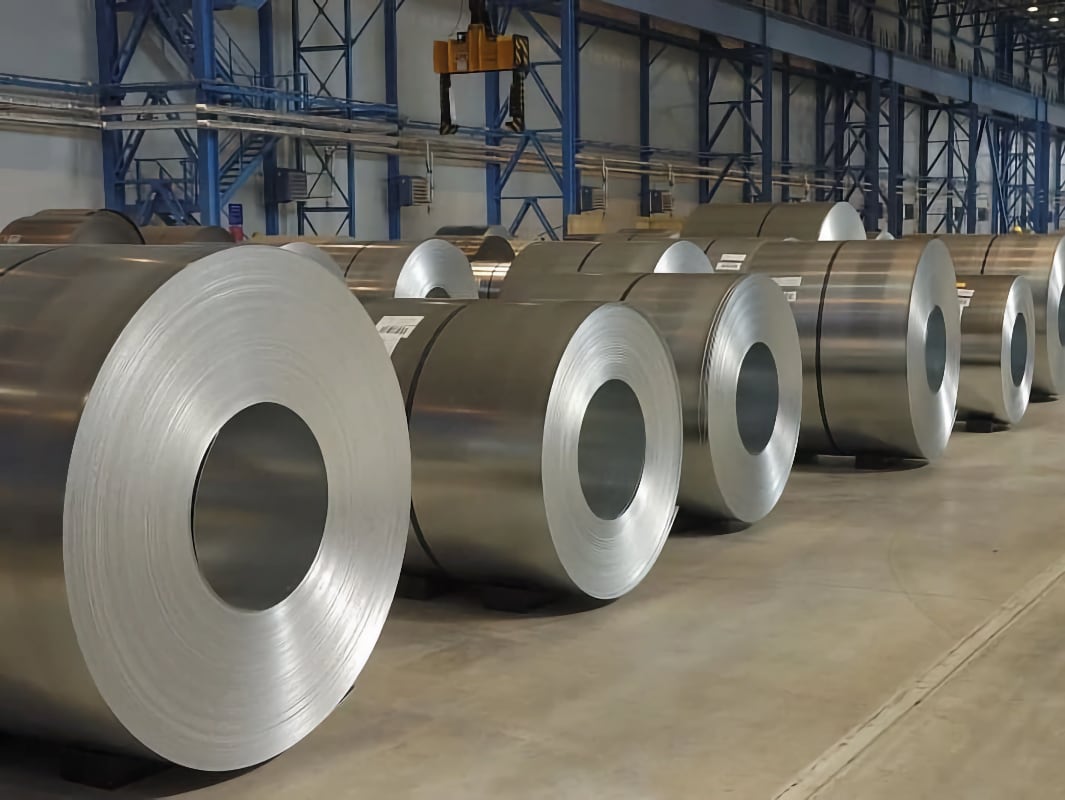 Великі рулони металу розміщені в промисловому складі з металевими стійками і крановими механізмами на задньому плані.