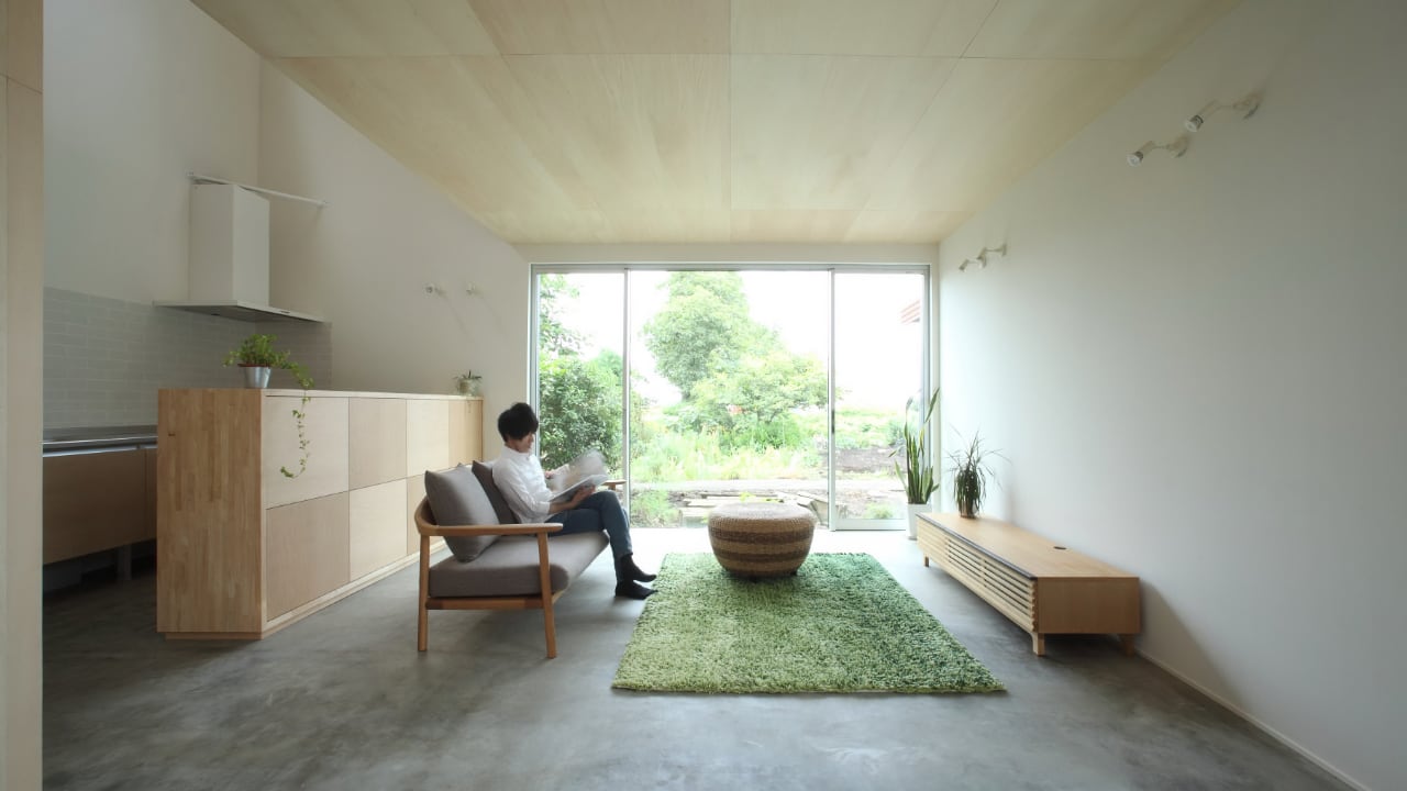 Японский интерьер комнаты с креслом, кухонным гарнитуром и видом на сад через большие окна.