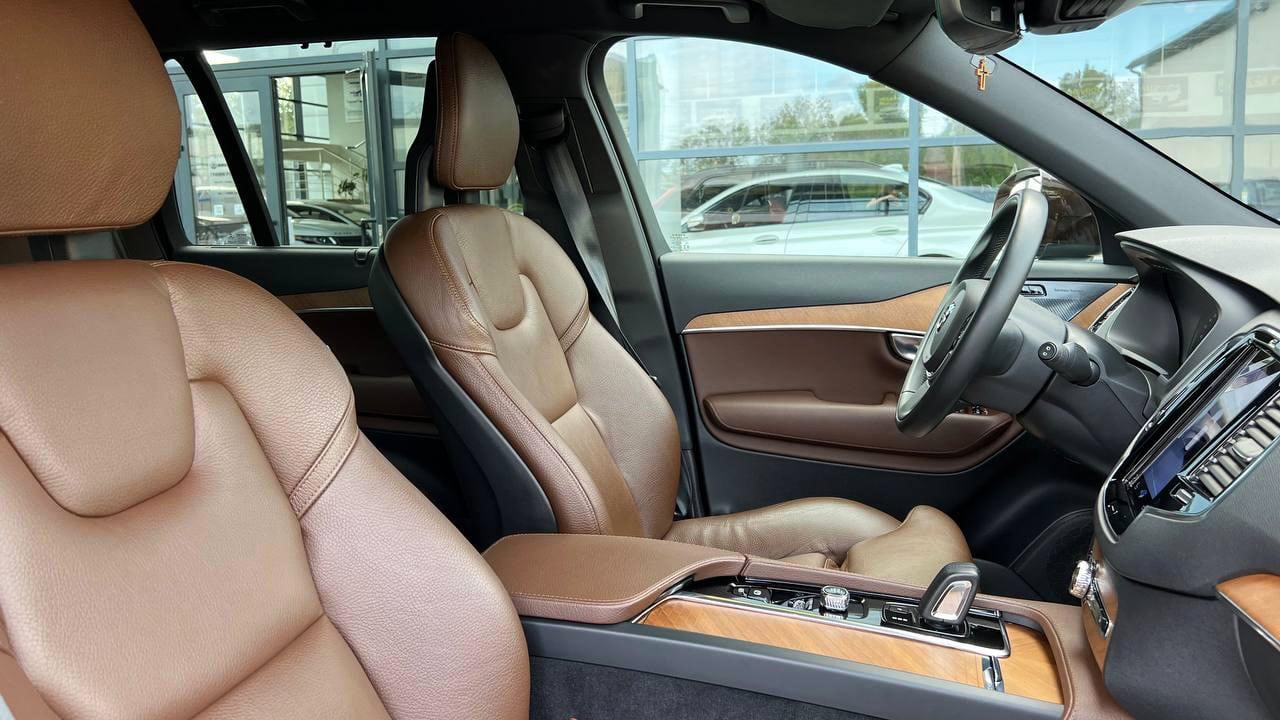 Интерьер автомобиля с коричневыми кожаными сиденьями, рулевым колесом, панелью приборов и деревянными вставками.