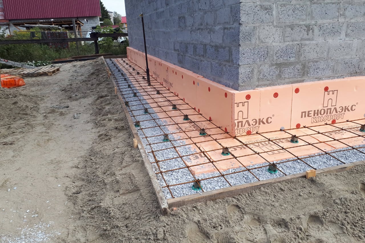 Стройплощадка: фундамент, арматурная сетка, пеноблоки, неотделанный блочный стен, песчаная основа.