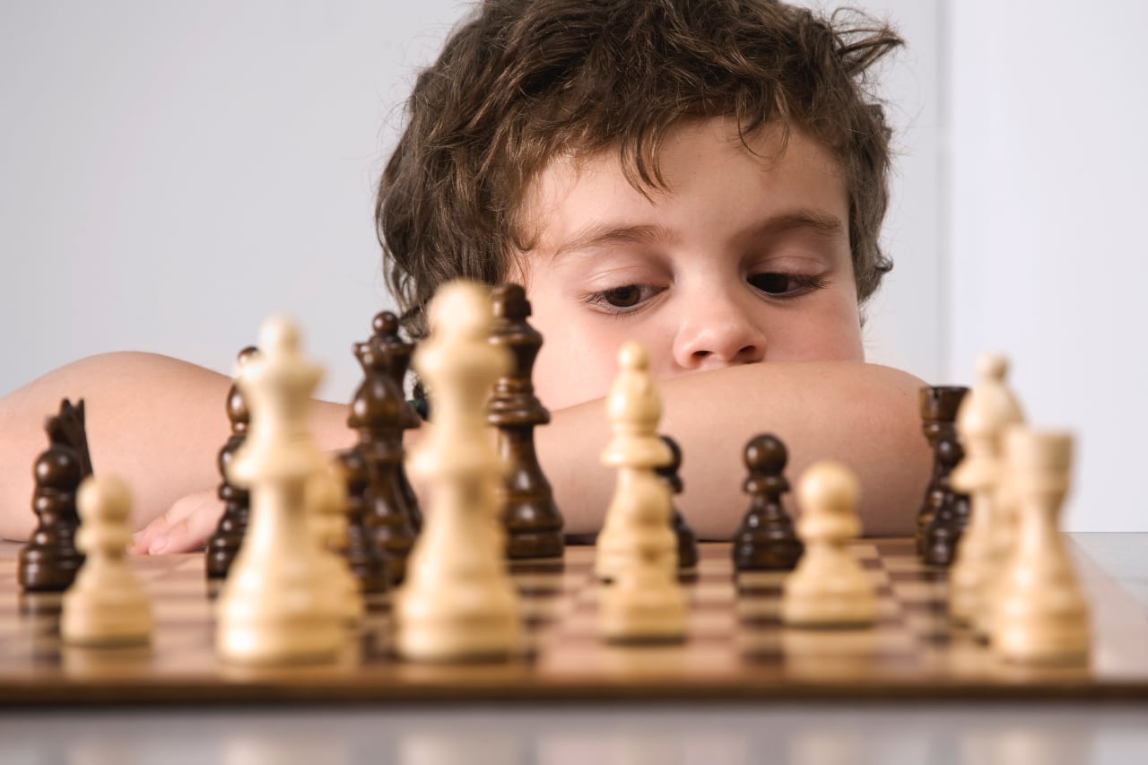 Хлопчик дивиться на шахівницю, розглядаючи фігури. Концентрація, роздум, стратегія, гра. Білі та чорні шахи, контемплетія.