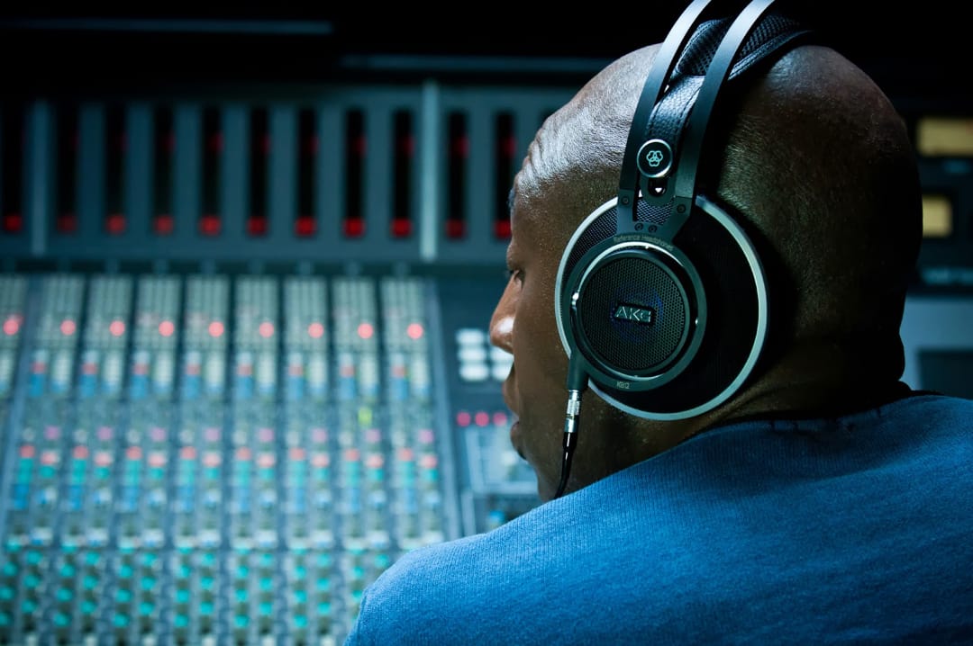 Людина в навушниках AKG працює за звуковим пультом мікшера з безліччю кнопок і червоними рівнями звуку