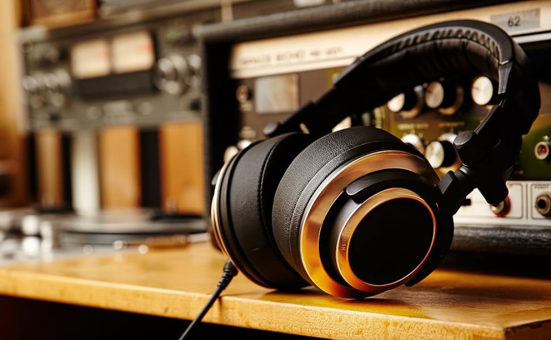 Навушники з м'якими амбушюрами у золотисто-чорному кольорі лежать на дерев'яній поверхні перед аудіо обладнанням