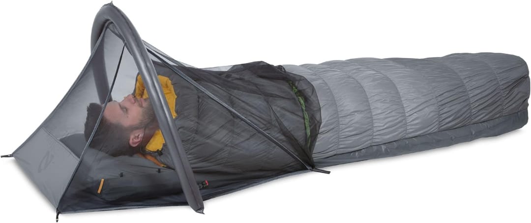 Мужчина спит в спальном мешке внутри одноместной палатки с сетчатым верхом на белом фоне, демонстрируя кемпинговое снаряжение.