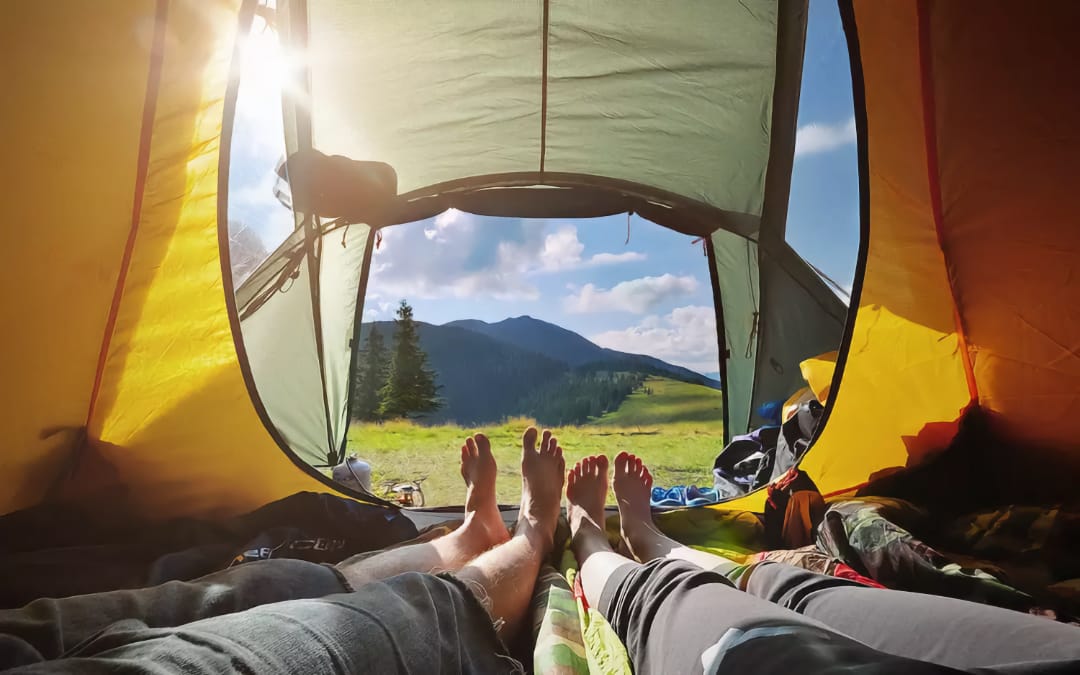 Вид изнутри палатки на горный пейзаж с ногами двух человек, отдыхающих внутри, на переднем плане.