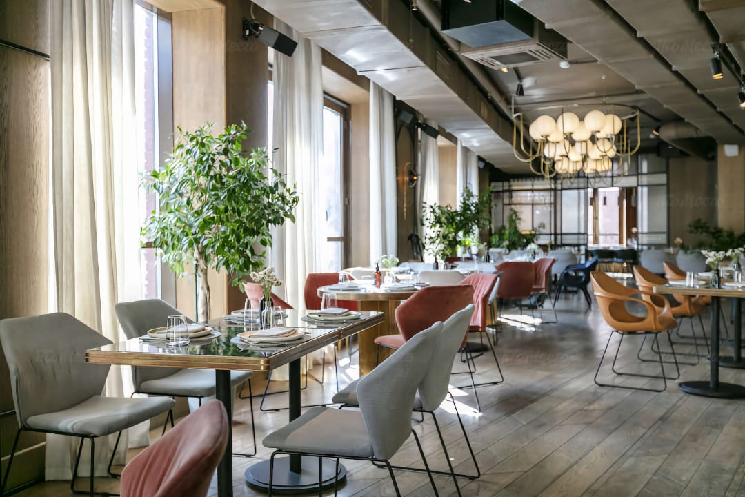 Зображення елегантного ресторану з натуральною дерев'яною підлогою, стильними стільцями та м'яким освітленням з підвісних світильників.