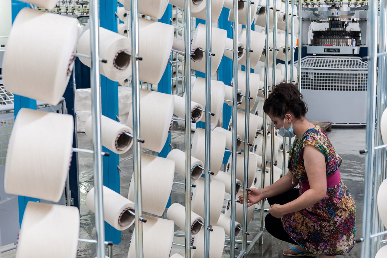 Женщина в цветастом платье, работающая с катушками ткани на текстильном производстве.