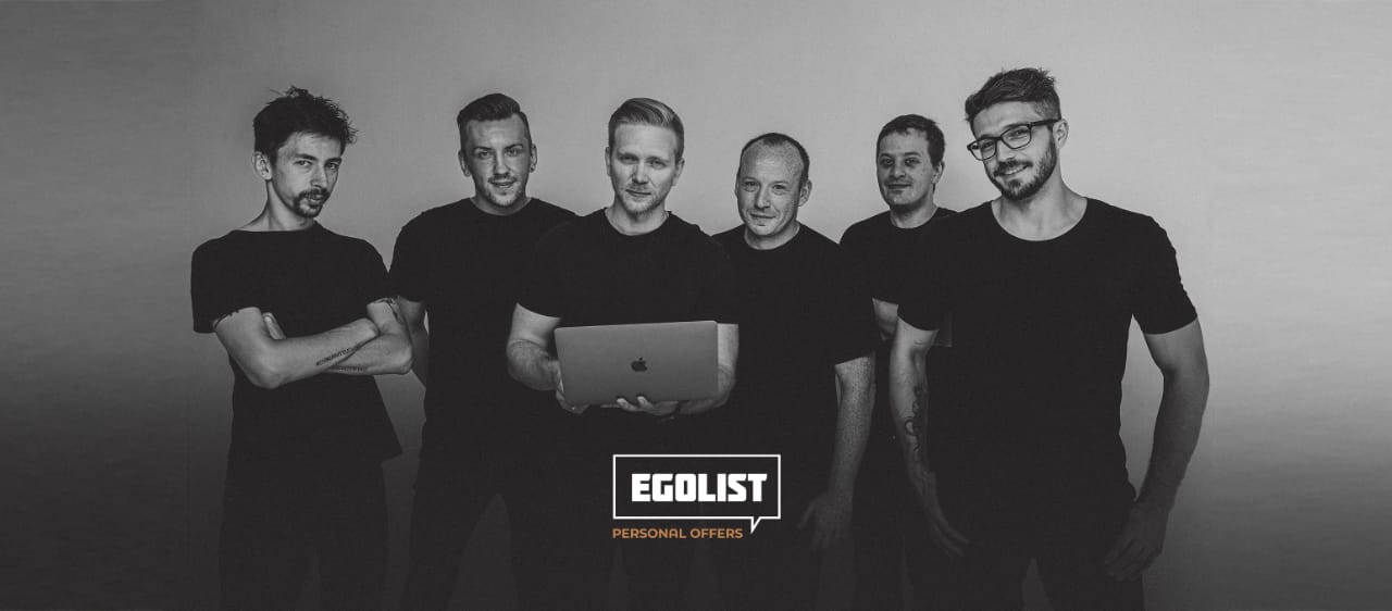 Группа из шести мужчин в черной одежде стоит рядом, держа ноутбук с логотипом "Egolist