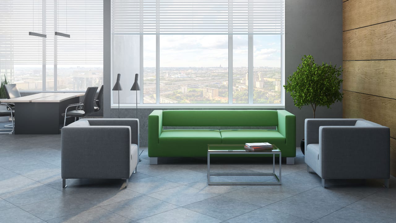 Просторий офіс з панорамними вікнами, зеленим диваном, сірими кріслами і скляним столиком, вид на місто.