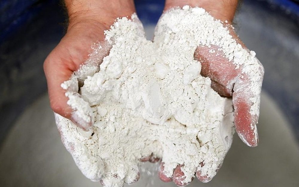 Руки человека загрязнены белым порошкообразным веществом, которое похоже на муку или глину. Руки держат это вещество и можно предположить, что это может быть процессом приготовления теста или работы с глиной для керамики.