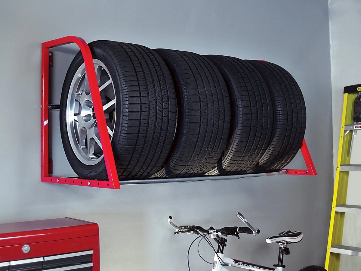 Гараж с красной стенной полкой для хранения шин, на которой расположены четыре черных автомобильных колеса. Рядом стоит велосипед и красный инструментальный ящик.