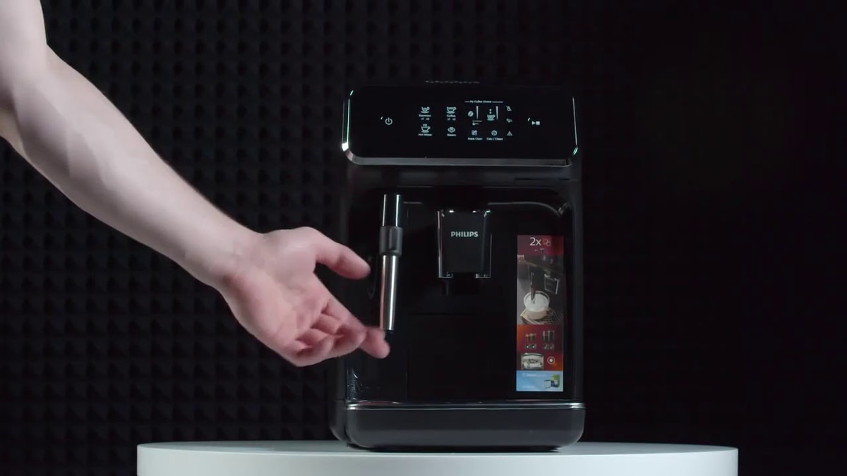 Изображена рука человека, управляющая современной кофемашиной Philips с цифровым дисплеем и множеством вариантов приготовления напитков