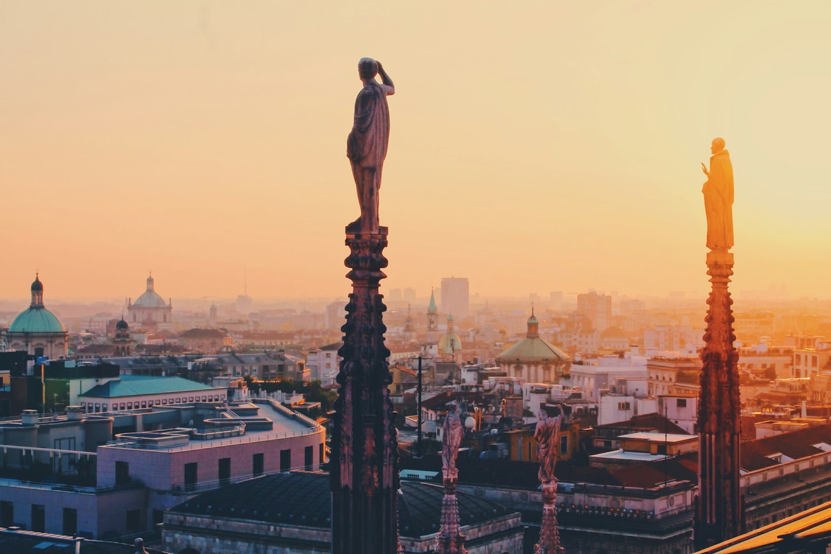 Зображення з видом на міський пейзаж заходу сонця з фігурами статуй, що дивляться на місто з даху будівлі в Італії.