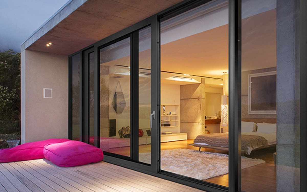 Современный интерьер дома с большими стеклянными дверями и видом на террасу с розовыми пуфами. Комната наполнена теплым освещением и уютной атмосферой, современная мебель и декор создают стильный и комфортный дизайн.