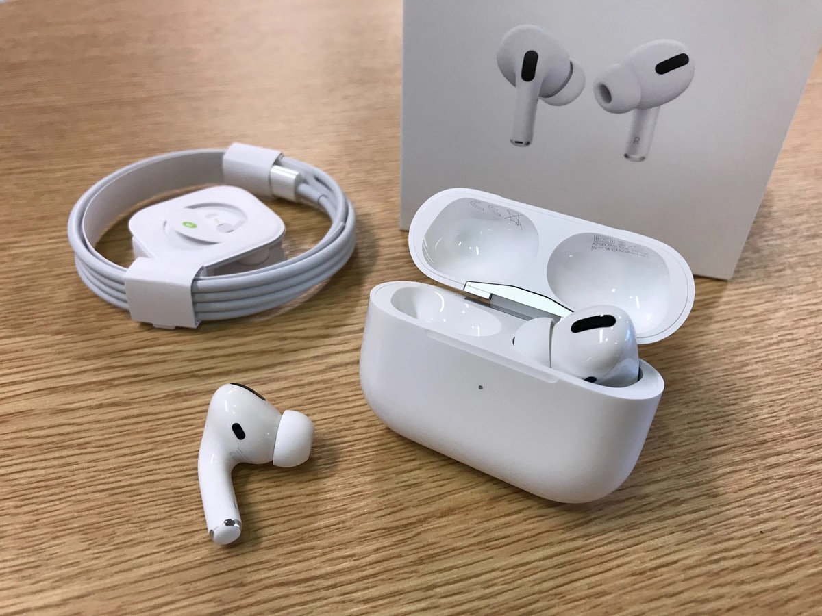 Комплект навушників AirPods Pro: зарядний кейс із відкритими навушниками, один навушник лежить поряд, зарядний кабель акуратно згорнутий на дерев'яному столі. Фон - упаковка пристрою.