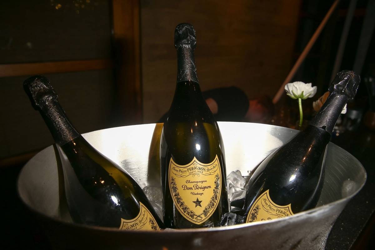 Три пляшки шампанського Dom Perignon Vintage, поміщені в металеве відерце з льодом, на тлі затишного інтер'єру з келихом та білою квіткою.