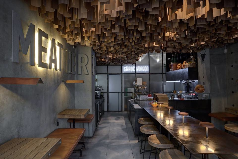 Фото гостевого зала ресторана с серыми стенами и полом, массивным баром и необычным потолком с тонкими деревянными пластинами различной длины 