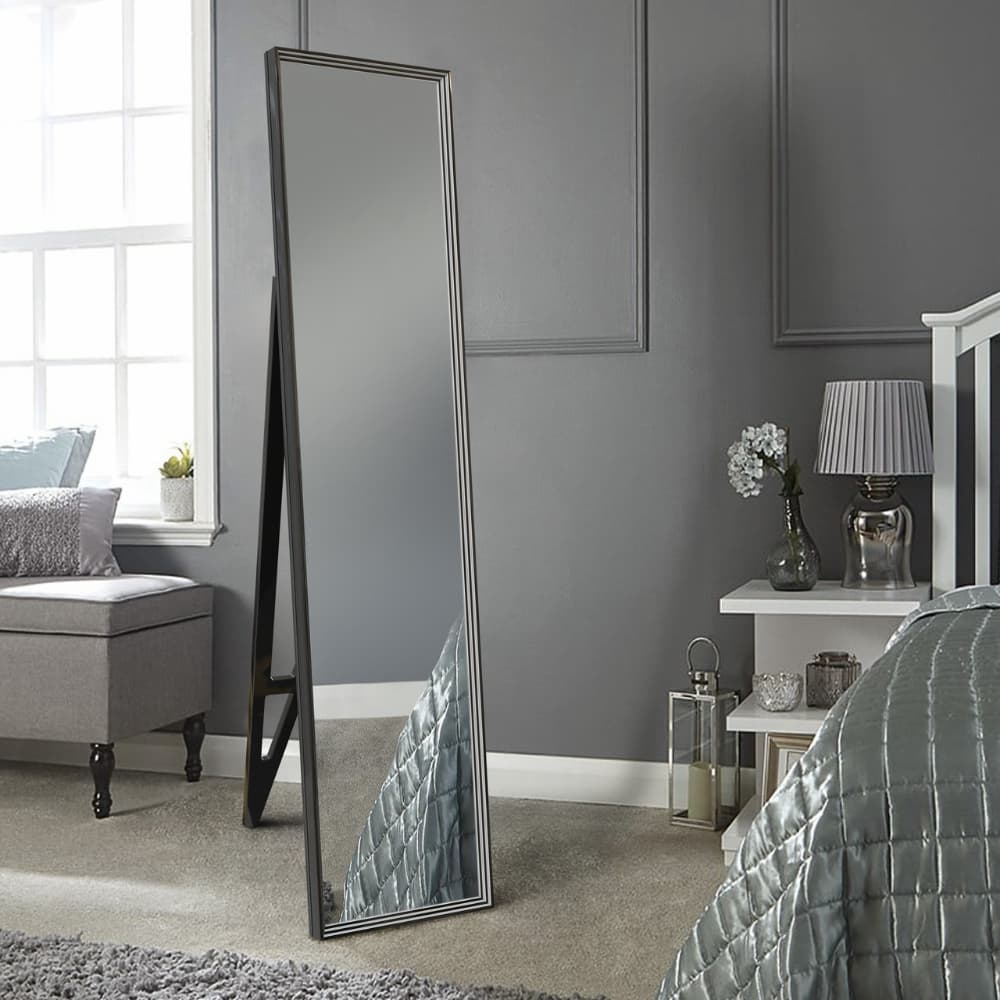 Стильне підлогове дзеркало з чорною рамою в елегантному інтер'єрі спальні на тлі сірої стіни.